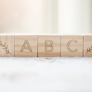 Pode incluir: Blocos de madeira com as letras A, B e C, cada bloco tem um pequeno desenho de folha em um lado.