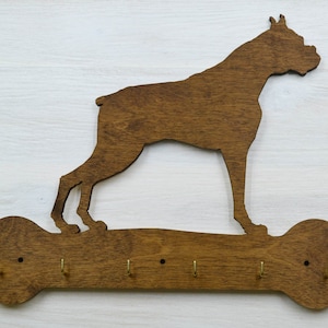 May include: Wooden key holder shaped like a dog standing on a bone. The dog is brown and the bone is brown with five gold hooks.