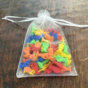 May include: A sheer white organza drawstring pouch filled with a collection of small, multi-colored plastic hand figurines. The miniature hands are rendered in vibrant shades of red, blue, yellow, green, and orange, each showing various gestures.