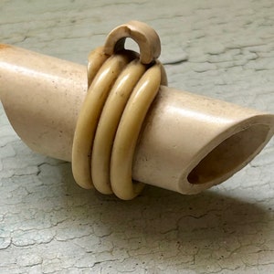 May include: A cream-colored, carved, wooden whistle with a loop at the top. The whistle is wrapped with a cream-colored cord.