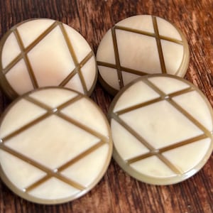 May include: Four round buttons featuring a cream-colored surface with a geometric pattern of intersecting brown lines. Each button has a smooth, polished finish and a raised brown border, creating a distinct grid-like design across the face.