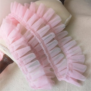 May include: Pink ruffled trim made of delicate tulle fabric. The trim is approximately 1 inch wide and has a soft, flowing texture.