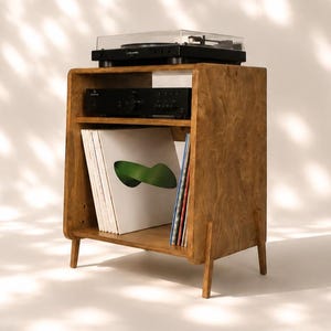 May include: A wooden record player stand with a natural grain finish, featuring a top surface for a turntable, a middle shelf for an audio receiver, and a bottom storage area for vinyl records, supported by four tapered legs.