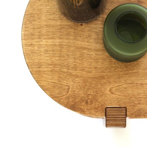 May include: A round wooden tray with a dark green glass vase and a small wooden block with a grooved texture.