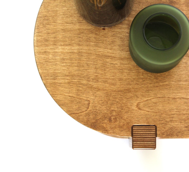 May include: A round wooden tray with a dark green glass vase and a small wooden block with a grooved texture.