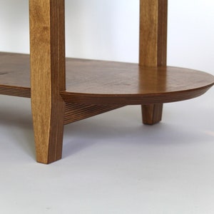 May include: A wooden shelf unit with two shelves. The shelves are oval shaped and the unit has four legs. The wood is a light brown color.