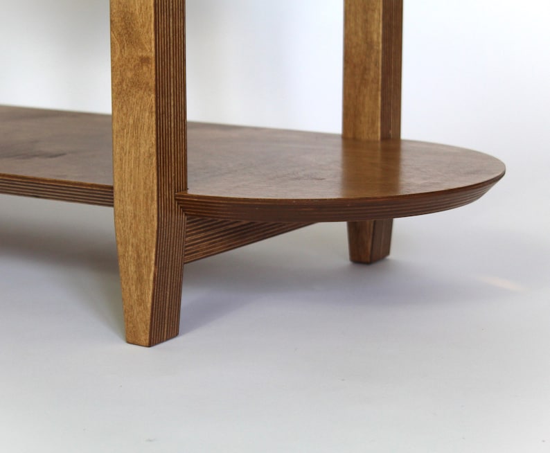 May include: A wooden shelf unit with two shelves. The shelves are oval shaped and the unit has four legs. The wood is a light brown color.