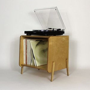 May include: A light wood record player stand with a clear plastic cover and a record player on top. The stand has a shelf for storing records and is on four legs.