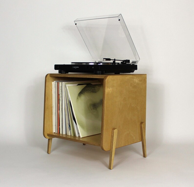May include: A light wood record player stand with a clear plastic cover and a record player on top. The stand has a shelf for storing records and is on four legs.