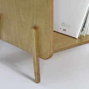 May include: A light wood record shelf with a curved front and four legs. The shelf is filled with vinyl records.