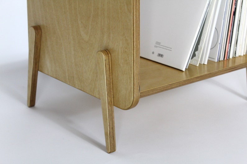May include: A light wood record shelf with a curved front and four legs. The shelf is filled with vinyl records.