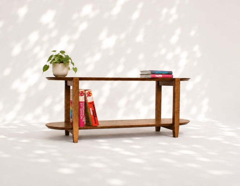 May include: A brown wooden console table with two horizontal shelves and four legs. A small green potted plant sits on the left side of the top shelf. Two books are stacked on the right side of the top shelf, and two books stand on the bottom shelf.