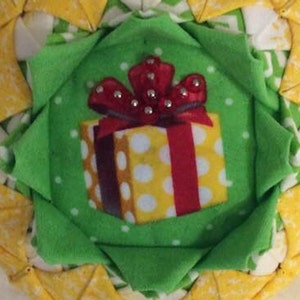 May include: A green fabric ornament with a yellow and white polka dot gift box with a red bow and silver embellishments.
