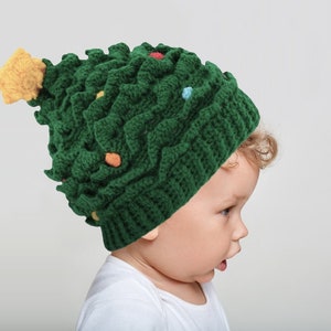 May include: A green knitted Christmas tree hat with colorful pom-poms. The hat is worn by a child with curly hair.