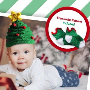 May include: A baby wearing a green and yellow knitted Christmas tree hat. The baby is lying on a white blanket with a red and white gift box in front of them. Free socks pattern included.