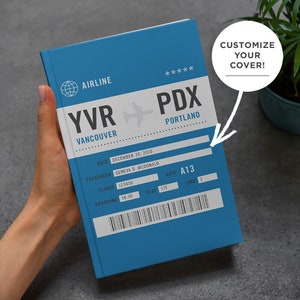 May include: Blue notebook with a boarding pass design. The notebook has the text "YVR - PDX" with "Vancouver" and "Portland" underneath. The date is December 20, 2020, the passenger name is Geneva D. McDonald, the flight number is 123456, the gate is A13, the seat is 17F, and the zone is 3. The text "Customize Your Cover!" is in a white speech bubble.