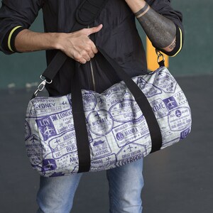 May include: A white and purple travel duffel bag with a black strap. The bag is covered in vintage-style stamps with city names and arrival and departure dates.