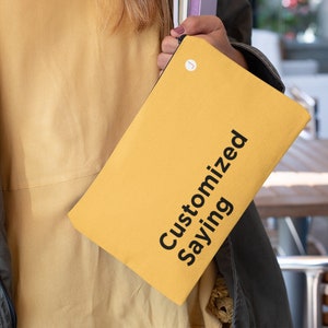 May include: A yellow canvas pouch with a black zipper and the text "Customized Saying" printed on the front.