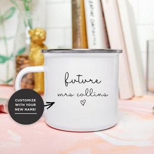May include: White enamel mug with a black inscription that reads "future mrs collins" with an arrow pointing to the right and a small heart symbol. The mug has a silver rim.