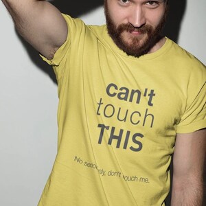 Könnte beinhalten: Ein gelbes T-Shirt mit dem Text "can't touch THIS" in Schwarz. Der Text "No seriously, don't touch me." ist in kleinerer Schrift unter dem Haupttext gedruckt.