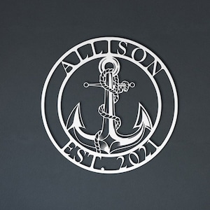 May include: A white metal anchor with rope design in a circle with the text "Allison Est. 2021" on a dark blue wall above a black and white patterned couch.