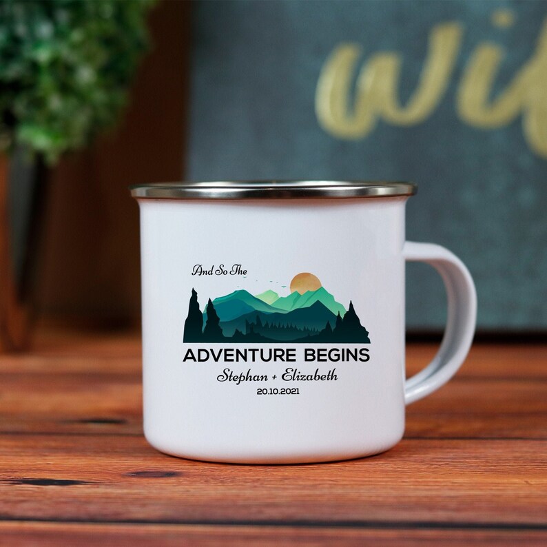 Op de afbeelding: Witte emaille campingmok met een berglandschap en de tekst "And So The Adventure Begins" met de namen "Stephan + Elizabeth" en de datum "20.10.2021".