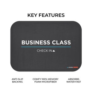 K&ouml;nnte beinhalten: Eine schwarze Badematte mit dem Text "BUSINESS CLASS CHECK IN" in Wei&szlig;. Die Matte hat einen blauen Streifen und den Text "ANTI-SLIP BACKING", "COMFY 100% MEMORY FOAM MICROFIBER" und "ABSORBS WATER FAST" in Wei&szlig;.