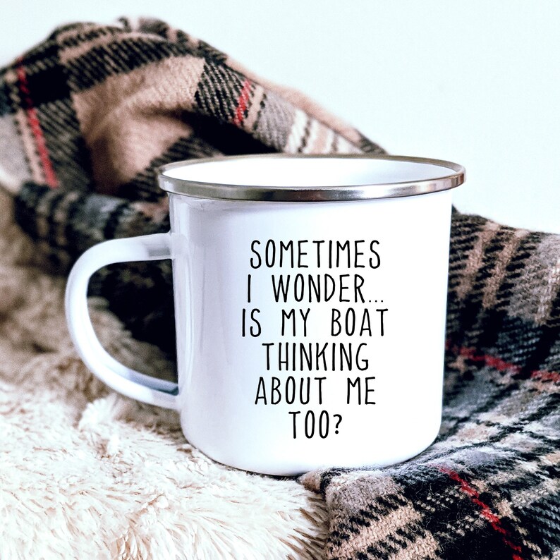 May include: White enamel mug with a silver rim and a black handle. The mug features the text "SOMETIMES I WONDER... IS MY BOAT THINKING ABOUT ME TOO?" in black lettering. The mug is set against a cozy, plaid blanket.