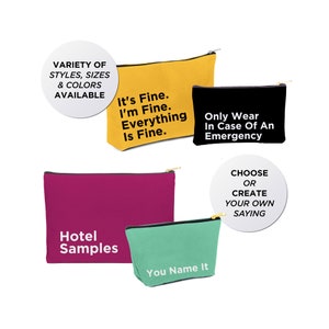 May include: Four different canvas zippered pouches with various sayings. The pouches are yellow, black, pink, and green. The sayings are "It's Fine. I'm Fine. Everything Is Fine.", "Only Wear In Case Of An Emergency", "Hotel Samples", and "You Name It". A white circle with black text says "CHOOSE OR CREATE YOUR OWN SAYING".