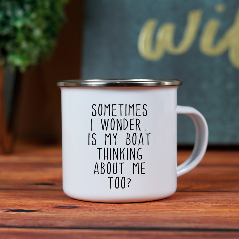 May include: White enamel mug with a silver rim and handle. The mug features the text "SOMETIMES I WONDER... IS MY BOAT THINKING ABOUT ME TOO?" in black lettering. The mug is on a wooden surface.