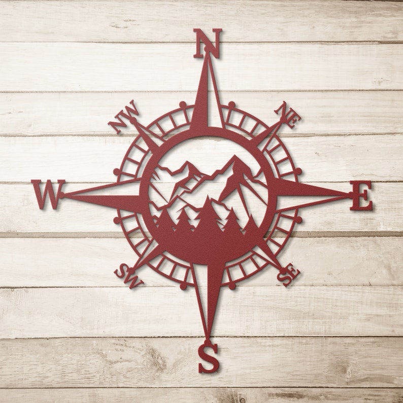 May include: A red metal compass with a mountain range design in the centre. The compass points north, south, east, and west. The compass is on a wood background.