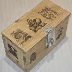 May include: A rectangular wooden box with a metal clasp and hinge. The box is decorated with black illustrations of characters from a science fiction franchise. The wood has a natural, light brown color.