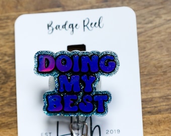 Pode incluir: Um carretel de crachá de glitter azul e roxo com o texto "Doing My Best" nele. O carretel de crachá está preso a um cartão branco com o texto "Badge Reel" e "Hot Mess Creative Shop" nele.