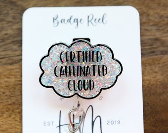 May include: A white glitter badge reel with a black cloud shape and the text "Certified Caffinated Cloud". The reel is attached to a silver retractable badge holder with a clear plastic charm.