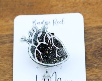 May include: A black and silver glitter heart-shaped badge reel with the text "Hot Mess Creative Shop" and "Badge Reel" on a white card.