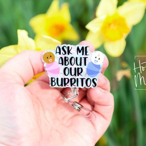 May include: A clear badge holder with a glittery background featuring two cartoon babies in swaddles. The text reads "Ask me about our burritos".