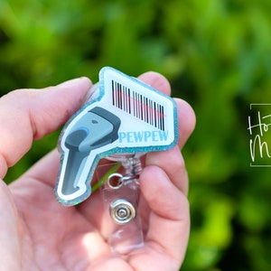 May include: A blue and white glitter badge holder with a barcode and the text "PEWPEW" on it. The badge holder is attached to a clear retractable badge reel.