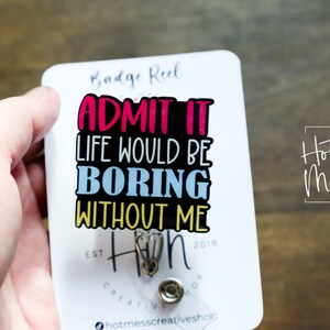 May include: White badge reel with a black background and colorful text that reads "Admit it, life would be boring without me." The text is in a fun, playful font. The badge reel has a silver retractable cord and a silver clip. The text "Hot Mess Creative Shop" is printed in the upper right corner.