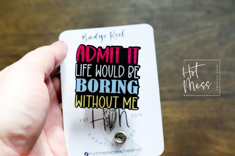 May include: White badge reel with a black background and colorful text that reads "Admit it, life would be boring without me." The text is in a fun, playful font. The badge reel has a silver retractable cord and a silver clip. The text "Hot Mess Creative Shop" is printed in the upper right corner.