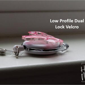 Puede incluir: Porta credenciales retr&aacute;ctil de color rosa con purpurina y cierre de velcro de doble cierre de perfil bajo. El porta credenciales tiene una correa de pl&aacute;stico transparente con un clip de metal. El texto "Hot Mess Creative Shop" es visible en la esquina inferior derecha de la imagen.