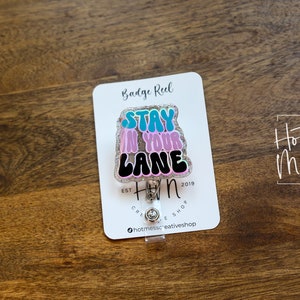 May include: A pink, blue and black glitter badge reel with the text "Stay in your lane" and the logo "Hot Mess Creative Shop" printed on a white card.