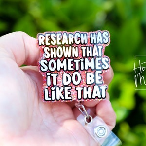 Op de afbeelding: Roze glitter badgehouder met een witte tekstoverlay die "Research has shown that sometimes it do be like that" luidt.