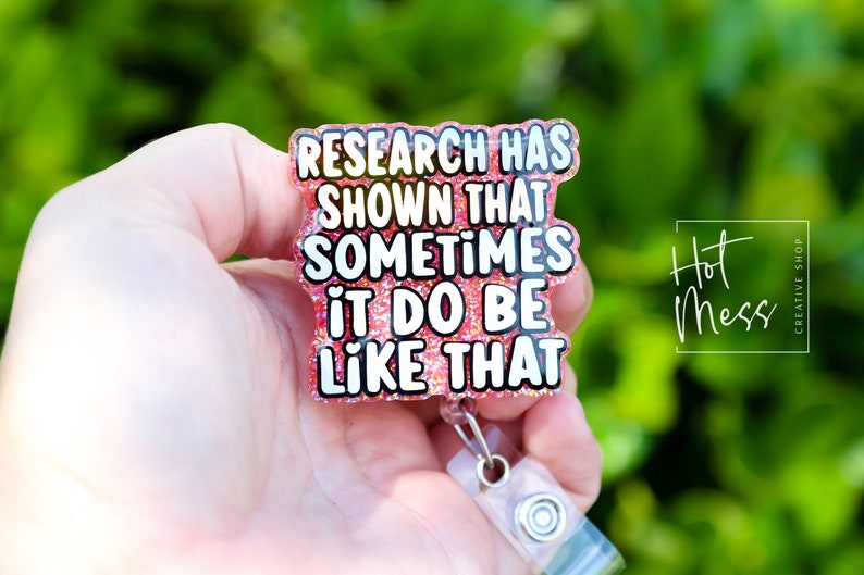 Op de afbeelding: Roze glitter badgehouder met een witte tekstoverlay die "Research has shown that sometimes it do be like that" luidt.