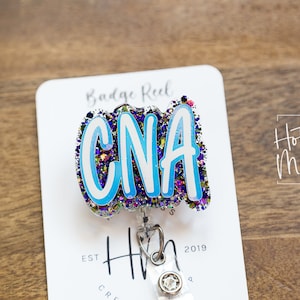 May include: A blue and white glitter badge reel with the text "CNA" in white letters. The badge reel is attached to a white card with the text "Badge Reel" and "Hot Mess Creative Shop" printed on it.
