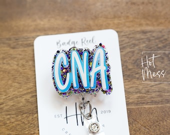 May include: A blue and white glitter badge reel with the text "CNA" in white letters. The badge reel is attached to a white card with the text "Badge Reel" and "Hot Mess Creative Shop" printed on it.