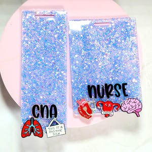 May include: Two rectangular badge holders with a glittery blue background. One says "CNA" with lung and sign graphics. The other says "nurse" with heart, uterus, and brain graphics. Both have a hole at the top.