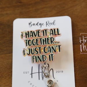 以下が含まれることがあります： ピンクと白のグリッターでできたバッジリールで、「全部揃ってるんだけど…見つからないのよね」という文字が書かれています。バッジリールは、「Badge Reel」と「Hot Mess Creative Shop」と書かれた白いカードに付いています。