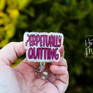 May include: A clear plastic badge holder with a pink glitter design that says "Perpetually Quitting".