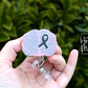 Könnte beinhalten: Ein rosa geformter Gehirnbadgehalter mit einem schwarzen Band im Inneren. Der Badgehalter ist an einer durchsichtigen, einziehbaren Badge-Rolle befestigt.