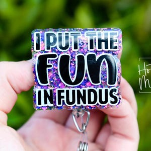 May include: A purple, pink, and blue glitter badge holder with a black and white text overlay that reads "I put the fun in fundus".